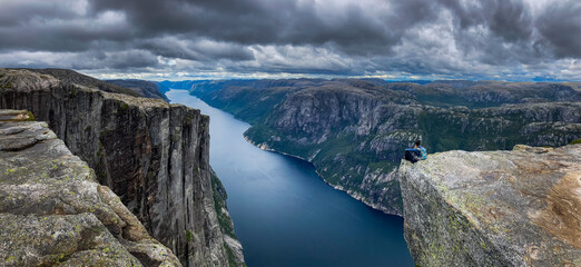 Eagle head viewpoint near Kjeragbolten Lysebotn Norway Young woman sits by the edge of the lysefjorden