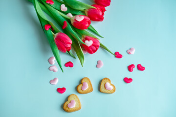 bouquet of red tulips with small heart-shaped cookies on a blue background, top view