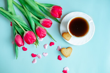 a cup of coffee in a white cup, with scattered hearts and red tulips on a blue background.