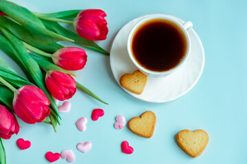 Fototapeta na wymiar a cup of coffee in a white cup, with scattered hearts and red tulips on a blue background.