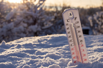 Thermometer on snow shows low temperatures in celsius or farenheit. On the Sunset
