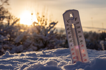 Thermometer on snow shows low temperatures in celsius or farenheit. On the Sunset