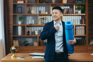 Businessman has finished his working day and is preparing for fitness, Asian is working in a classic office, late, man is holding a mat for fitness