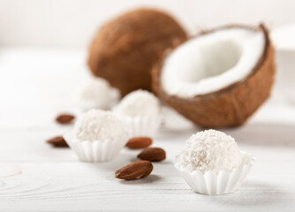 Coconut candies. Coconut balls in a light package on a white textured wood. Homemade vegan sweets.Closeup view, place for text. Tasty white bliss balls. Candies with butter cream and almonds.