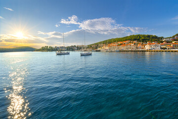 Late afternoon sunlight on the Dalmatian Coast of the Adriatic sea with boats in the harbor and a small town near the island of Hvar along the coast of Croatia during summer. - obrazy, fototapety, plakaty