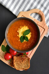 A plate of tomato soup on a black background. Tomatoes, greens, wooden board. View from above. 