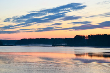 The river reflects the sky at dawn, a dark strip of forest and fog on the far shore