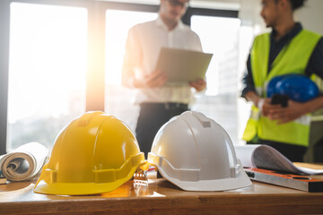 Close up yellow safety helmet on the table and contractor and customer shaking hands after confirm...