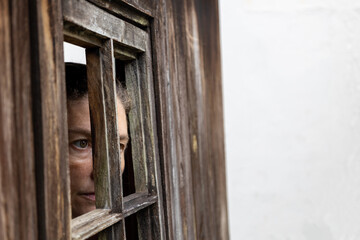 woman  staring out of a broken wooden window with copyspace