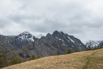 Atmospheric landscape with large thorny dragon shaped mountain top under gray cloudy sky. Gloomy top view from hill to high snowy mountain range with sharp rocks in shape of dragon back in low clouds.