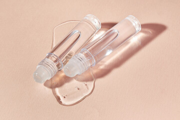 Transparent lip gloss in a roller ball bottles on a beige background. Decorative cosmetic lipstick. Beauty makeup product 