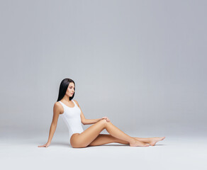 Attractive and slender brunette girl in white underwear posing in studio. Healthy lifestyle, sport and body care concept.