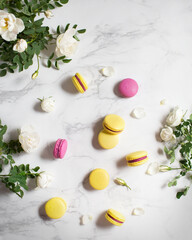 Fototapeta na wymiar Macaroons and flowers. French food. Yellow and pink macaroons on a marble table. French dessert and white flowers.