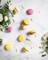 Macaroons and flowers. French food. Yellow and pink macaroons on a marble table. French dessert and white flowers.