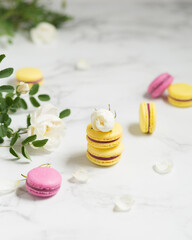 Obraz na płótnie Canvas Macaroons and flowers. French food. Yellow and pink macaroons on a marble table. French dessert and white flowers.