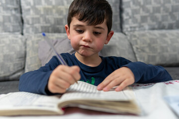 Young child entertained resolving the crossword puzzles at his grandmother's house. Pensive boy trying to solve crosswords with the pen.