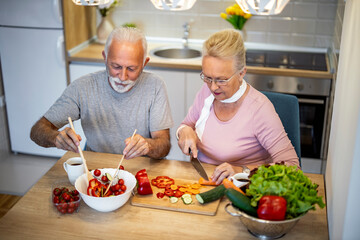 Happy senior couple preparing fresh vegetable salads