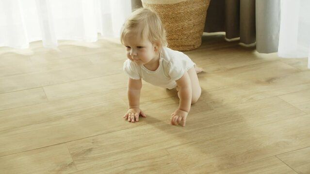 Cute Happy Little Toddler Baby Girl Is Crawling On A Wooden Floor At Home. Exploring Home, Child Smiling, Concept Of Love, Family, Newborn, Childhood, New Life And Parenthood. Slow Motion