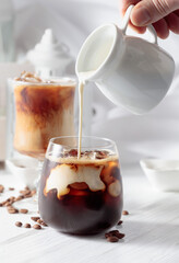 Cream is poured into a glass with iced coffee.