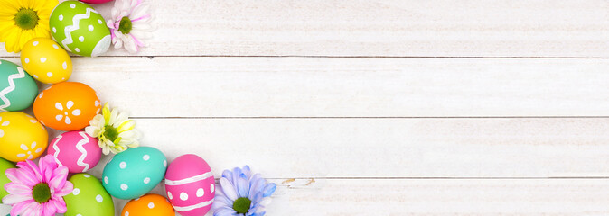 Colorful Easter eggs and spring flowers. Top view corner border against a white wood banner background. Copy space.