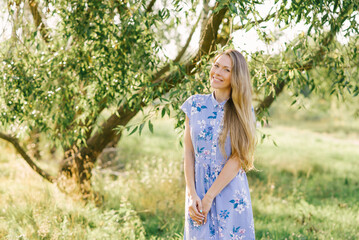 Fototapeta na wymiar Cute young woman in a blue dress smiles while walking in the park