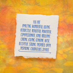 positive affirmation with a long list of words - handwriting on a small sheet of handmade paper against orange and yellow marbled paper