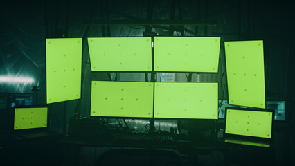 Modern computers with green screens placed on desk in dark room with shimmering lamps on illegal...