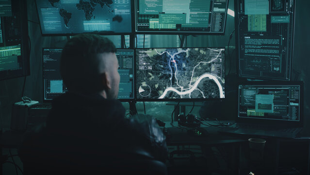 Zoom in view of anonymous man using illegal software on computer while spying on victims with associates in dark room at night