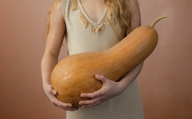 Little girl holding a Halloween pumpkin on a pink background.
Autumn fall concept.
Pumpkin in female hands.