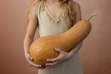 Little girl holding a Halloween pumpkin on a pink background.
Autumn fall concept.
Pumpkin in female hands.