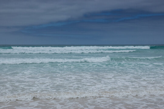 The turquoise, blue and green waves of the sea hit the white sands of the beach at Tortuga Bay, Galapagos Islands.