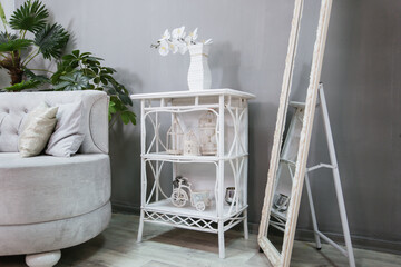 The interior is in white and gray tones with a vintage bedside table, a mirror, a gray sofa and green plants.