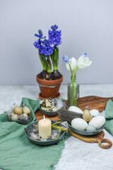Dekoration Ostern mit Eiern, Federn und Frühlingsblumen auf einem Tisch mit Teller, Schale, Blumenvase und Holzbrett, Frühling dekorieren, Tulpe, Hyazinthe
