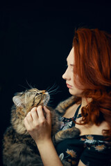 Portrait of young woman holding cute siberian cat. Red-haired female hugs and strokes fluffy pet. Happy pussycat in arms of beautiful girl. Love and affection for domestic animals.