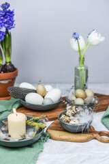 Dekoration Ostern mit Eiern, Federn und Frühlingsblumen auf einem Tisch mit Teller, Schale, Blumenvase und Holzbrett, Frühling dekorieren, Tulpe, Hyazinthe
