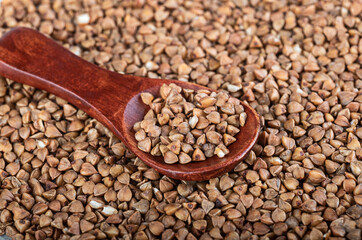 Wooden spoon with buckwheat on a hill of buckwheat. Close-up. Blurred background