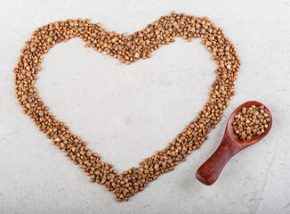 Buckwheat, poured in the shape of a heart and a wooden spoon with buckwheat on a beautiful gray background