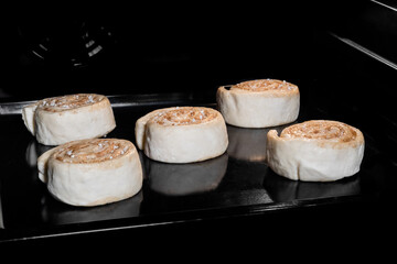 Five uncooked cinnamon buns on tray in electric oven, black background. Swedish cuisine, homemade bakery, food, cooking, pastry, semi-finished products and raw concept