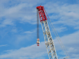 The mechanical arm of a self-propelled crane with hook and pulley suspended in the void