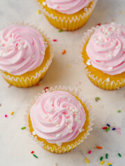 View from above. Cupcakes with whipped pink cream on a white background and colorful confetti. Festive composition. Birthday, celebration, family holiday, romantic date, dessert.