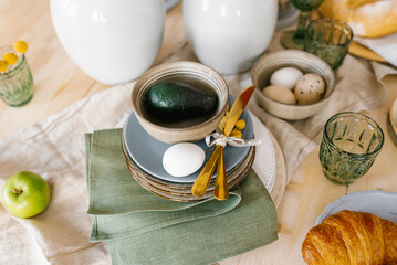 Easter festive spring table setting decoration, green napkins, eggs, apple, avocado in a plate, selective focus