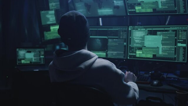 Hacker in virtual reality helmet in cyberspace located on secret hacker base with servers and multiple monitors during massive cyber attack. Trying to hack data or steal money in the meta universe
