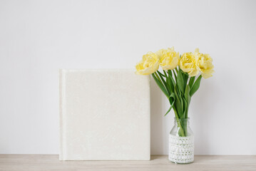 White family or wedding photo album with empty space for text and a bouquet of yellow tulips in a vase on the table. Family photo archive