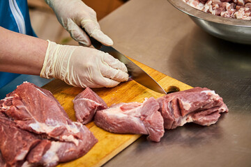 Cook cutting raw pork meat on wooden board in kitchen