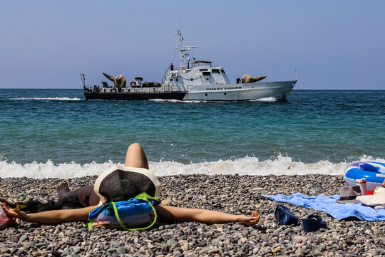 A Patrol Boat On The Horizon (coast Guard), And A Sunbathing Girl In A Hat On A Blurred Foreground