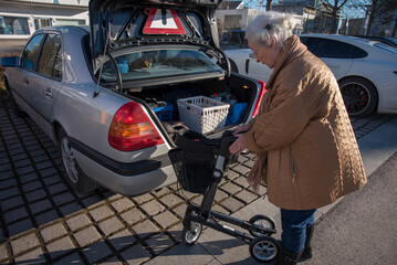 Senior woman folding rollator at car trunk - 486774918