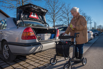 Senior woman with rollator loading foot in car trunk