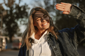 Cute young caucasian woman covers her face with hand while hiding from sun in open space. Blonde...