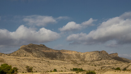 Colina árida sin vegetación con enormes cumulus de nubes bajas con cielo azul