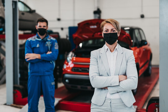 A businesswoman in a modern car repair shop is waiting for a mechanic to fix his car.  Mechanic and client are wearing protective face masks due to Covid-19 pandemic.